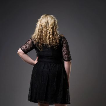 Woman with curly blonde hair in a black lace dress, seen from behind.