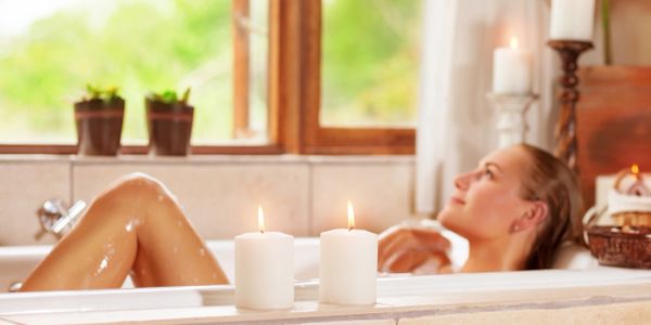 Lady in bath looking out the window with candles, plants, water, hair, basket 