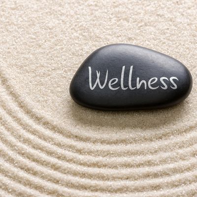 A black stone with 'Wellness' written on it, placed on raked sand.