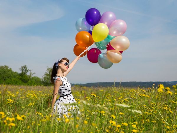 Woman in a polka-dot dress holding colorful balloons in a flower field.