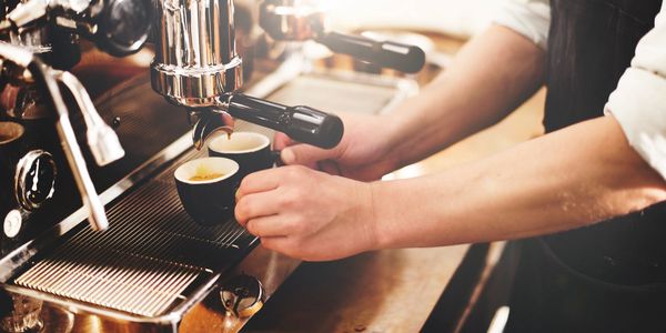 A barista making two cups of coffee using an espresso machine.