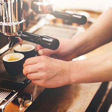 Hands preparing espresso shots with a professional coffee machine.