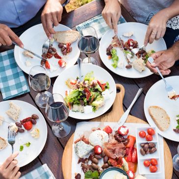 Friends sharing a Mediterranean meal with wine and fresh salad outdoors.