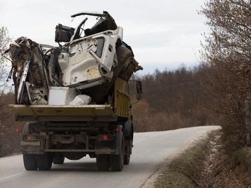 a dump truck filled with junk driving on a narrow road