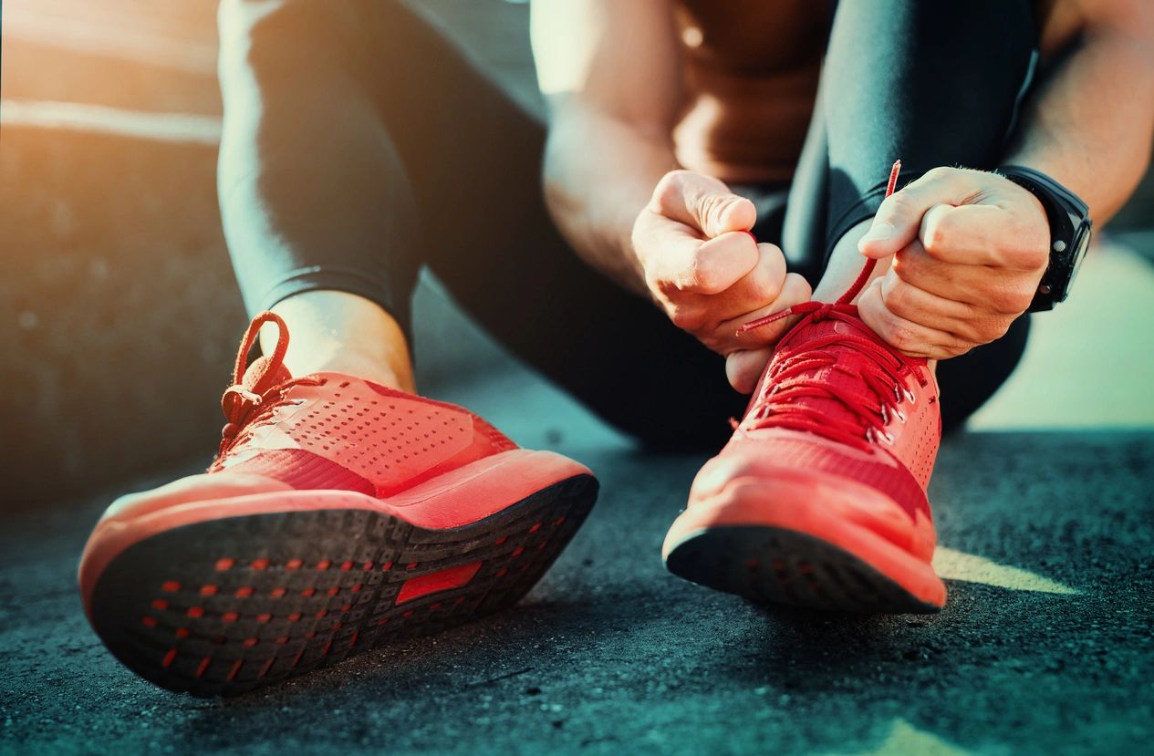 A person laces up their red sneakers as the sit on the pavement in their track performance gear.