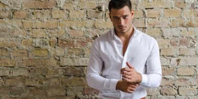 Hombre con camisa blanca frente a pared de ladrillos.