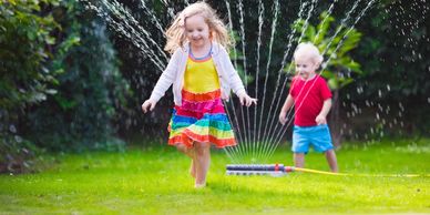 Two children playing in the garden sprinkler.