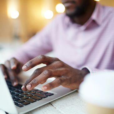 Black male wearing a pink shirt and typing on a laptop
