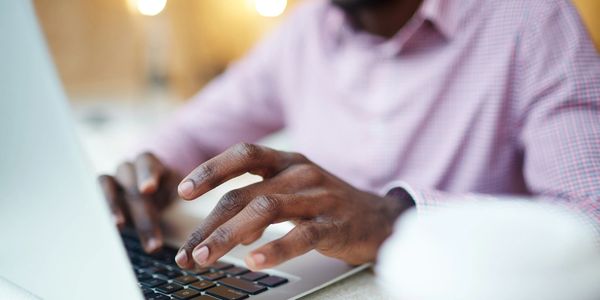 Man's torso shown as he uses a laptop. Face is not visible, his hands are typing on the keyboard. 