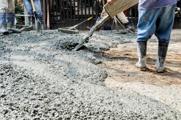 Workers pouring and spreading wet concrete on a construction site.