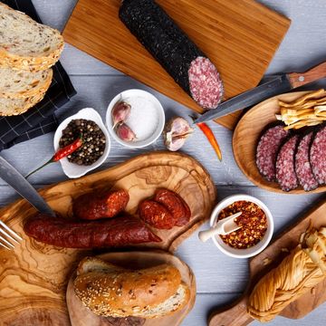 Charcuterie spread with sausages, sliced salami, bread, and spices on wooden boards.