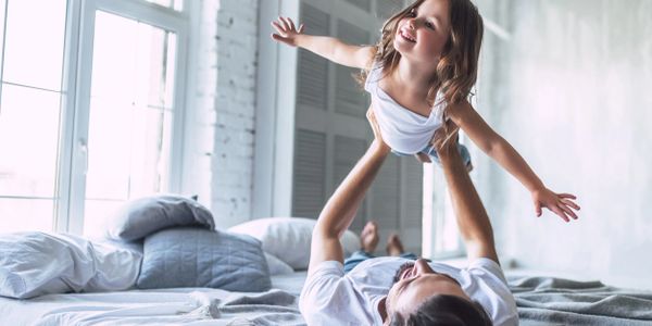 Parent laying on bed lifts child in the air like an airplane
