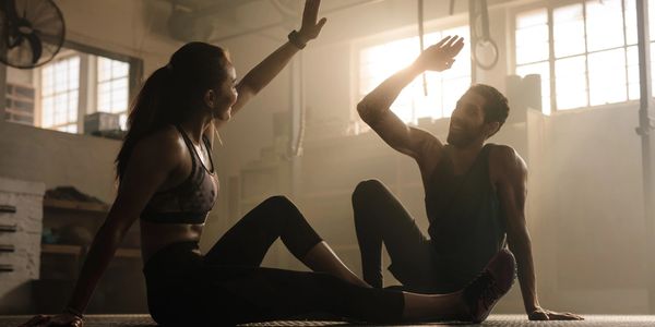 Two people high-fiving after a workout in a sunlit gym.
