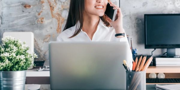 Woman smiling while on phone at her desk with laptop.