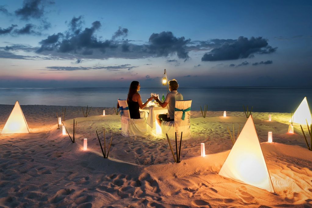 Romantic beach dinner setup with glowing lights at dusk.