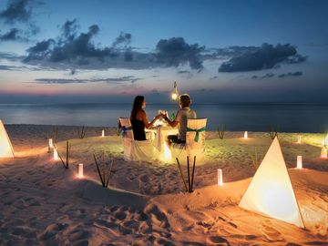 Couple dining romantically on the beach at sunset surrounded by lanterns.