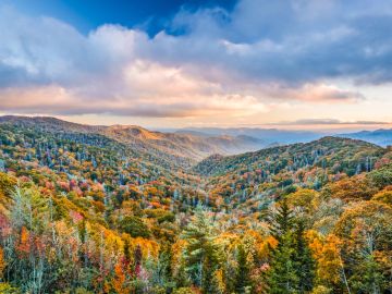 Scenic autumn landscape of rolling hills with colorful fall foliage under a partly cloudy sky.
