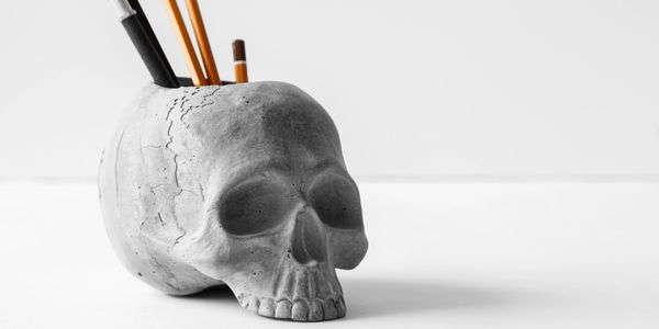 A skull pen holder with an assortment of writing utensils.