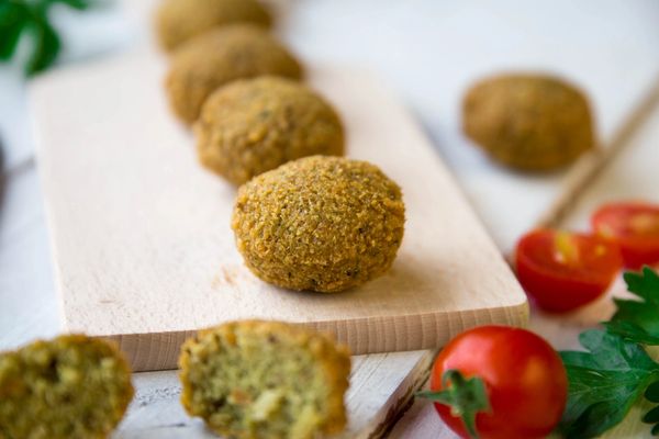 Golden falafel balls on a wooden board with fresh tomatoes and parsley.