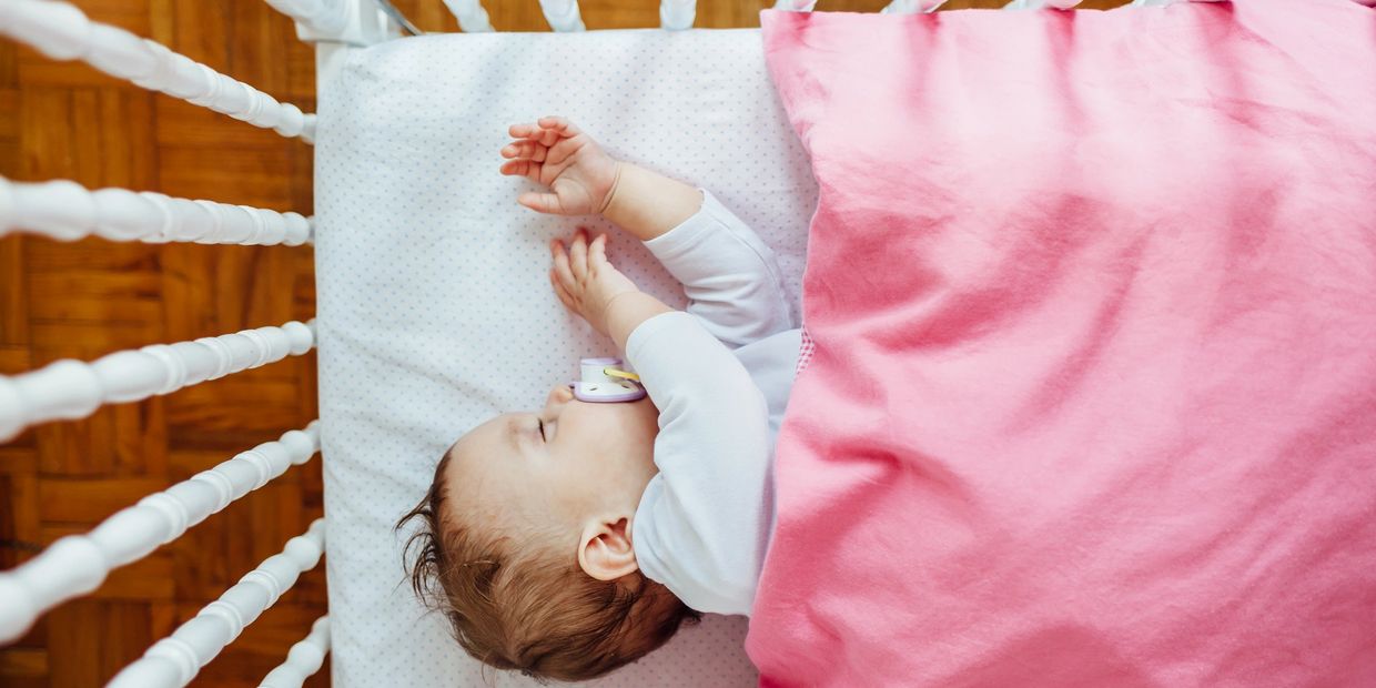 Sleeping baby with pink blanket in cot.