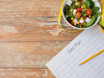 A healthy salad bowl with a diet plan sheet and pencil on wooden table.