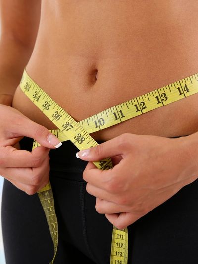 Person measuring their waist with a yellow tape measure.