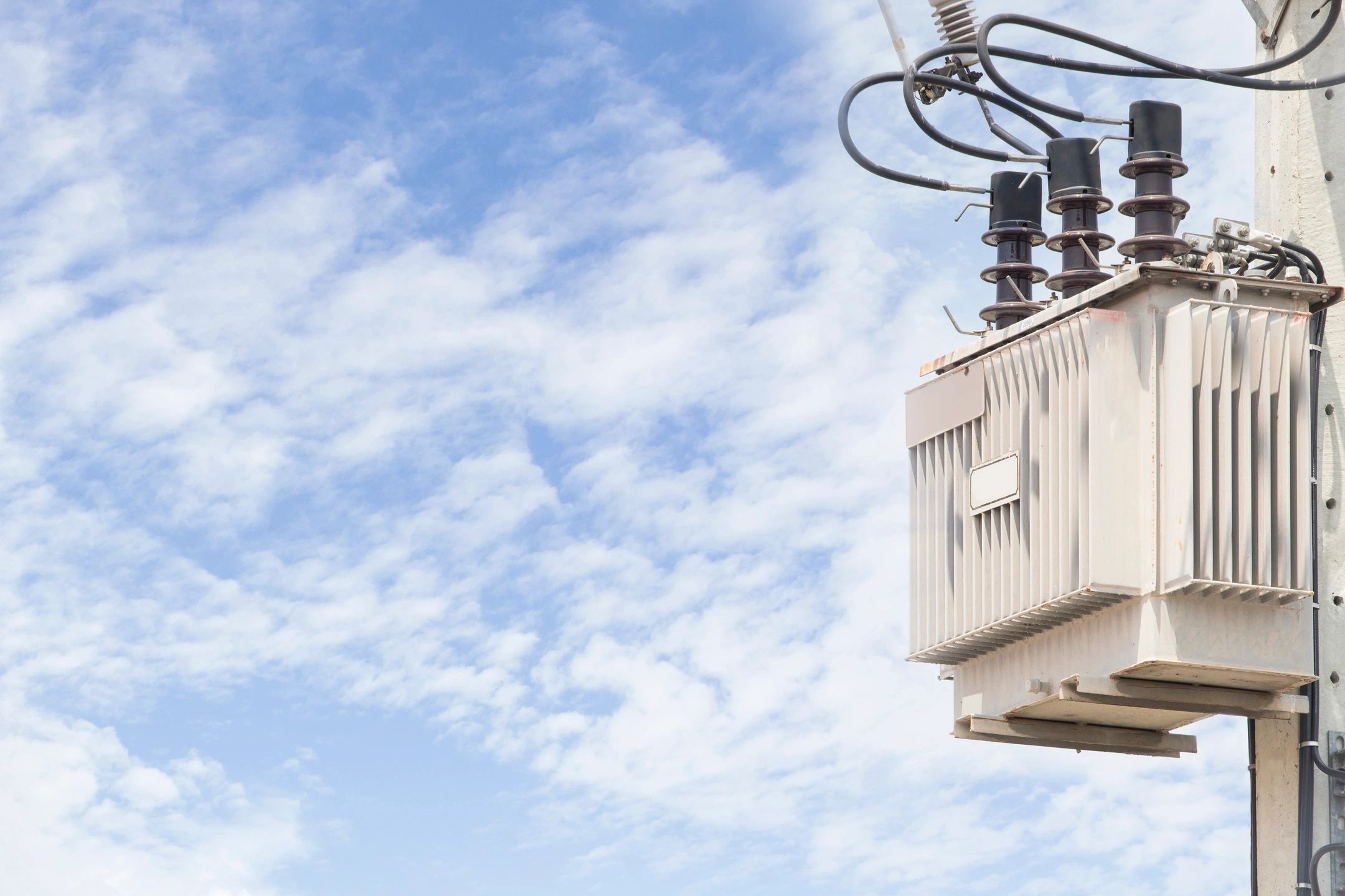 Electrical transformer mounted on a utility pole against a partly cloudy sky.