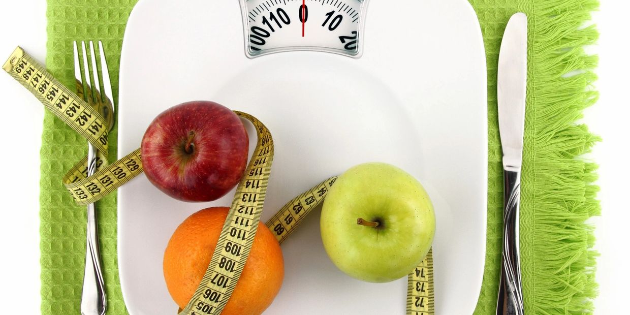 Fruits and measuring tape on a scale, symbolizing diet and weight management.