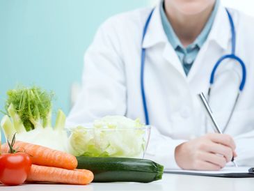 Doctor writing notes with fresh vegetables in the foreground.