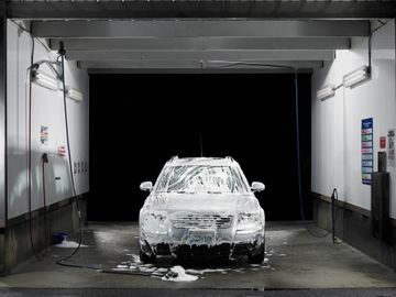 A car covered in soap foam at a self-service car wash bay.
