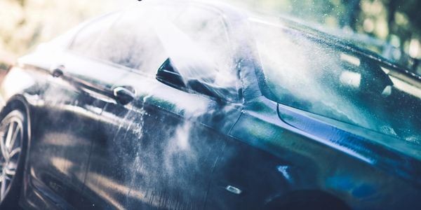 A shiny car being washed with a high-pressure water spray.
