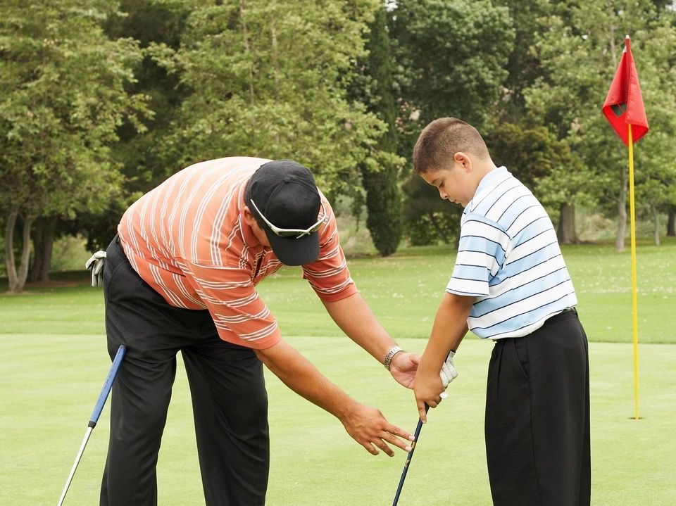 A man teaching a boy how to play golf on a putting green.