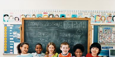 A diverse group of kids smiling in front of a math lesson chalkboard.