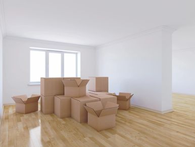 Empty room with stacked and open cardboard boxes on wooden floor.