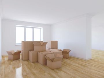 Empty room with stacked cardboard moving boxes near window.
