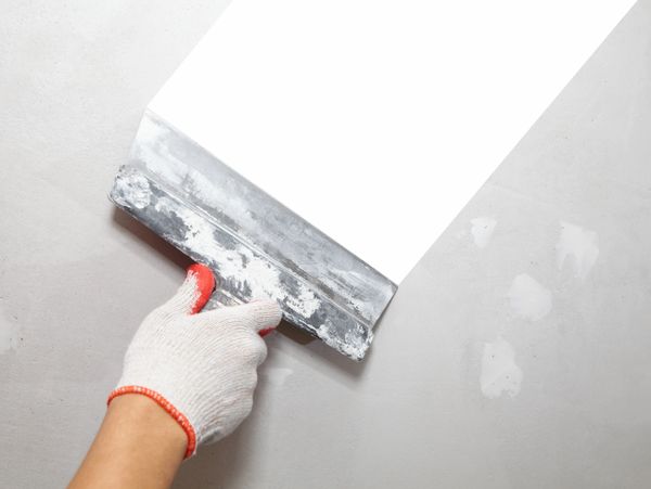Hand in glove spreading white plaster on a wall with a putty knife.
