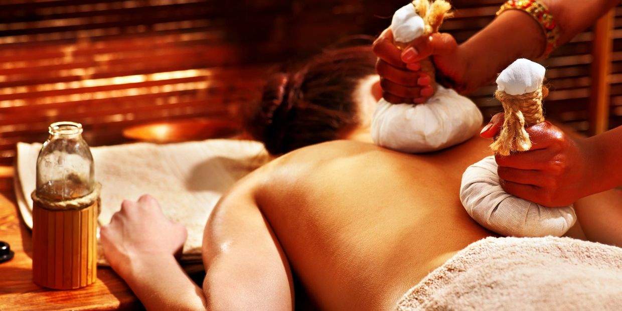 Person receiving a herbal compress massage on their back in a spa setting.