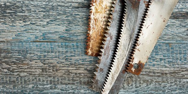 Three rusty saw blades on worn blue wooden surface.