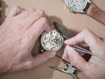Hands repairing a watch mechanism with tools.