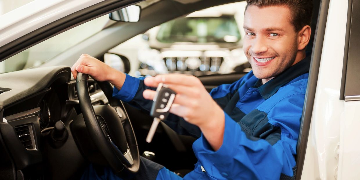 Man in blue uniform holding car keys, sitting in a car.