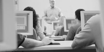 People attending a computer training class with a teacher at the front.