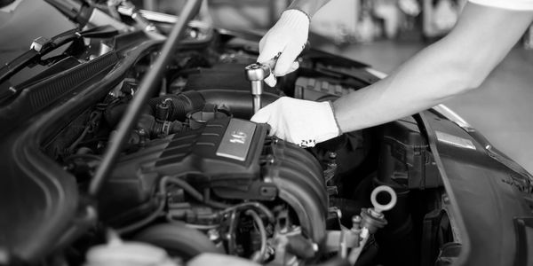 Mechanic using a wrench to fix a car engine wearing gloves.