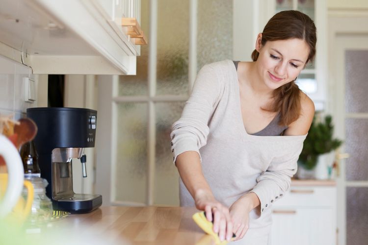A woman cleaning a kitchen countertop with a sponge, smiling gently.