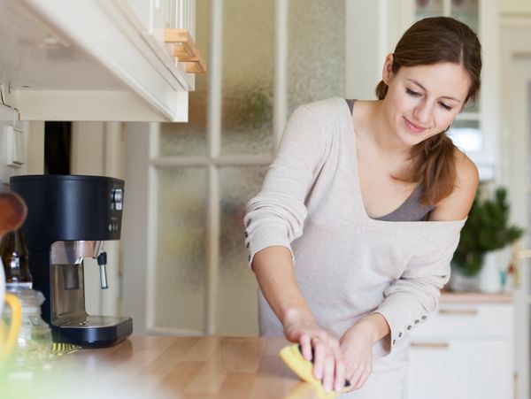 A woman cleaning a wooden kitchen countertop with a yellow cloth.