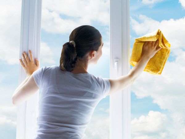 Woman cleaning a window with a yellow cloth on a sunny day.
