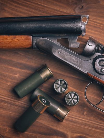 A break-action shotgun with shotgun shells on a wooden surface.