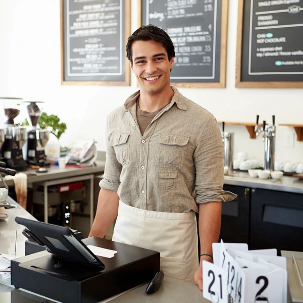 A man standing at a cash register at a coffee shop.