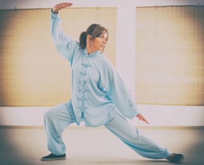 Woman practicing Tai Chi in light blue traditional attire indoors.
