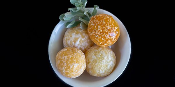 Four round pastries in a white bowl with a green garnish on a black background.