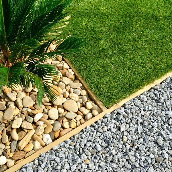 A garden section with green grass, smooth stones, and gravel separated by wooden borders.